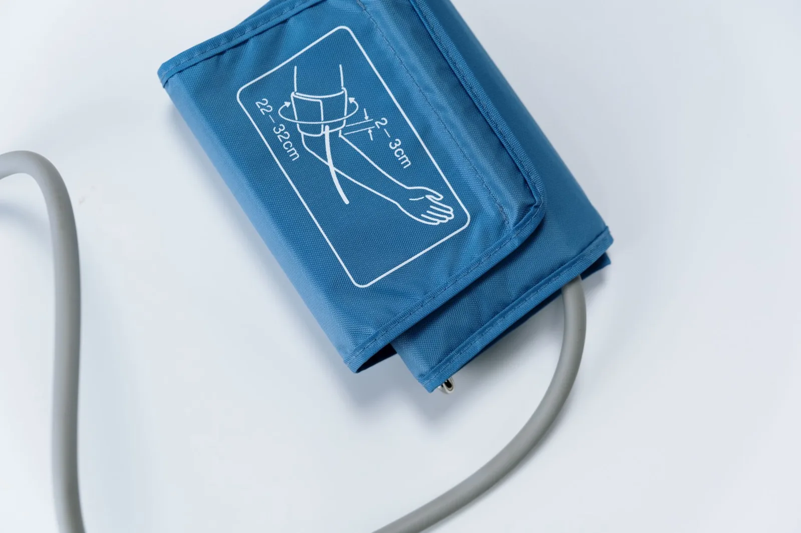 A blue blood pressure cuff and its tubing resting on a plain white surface.