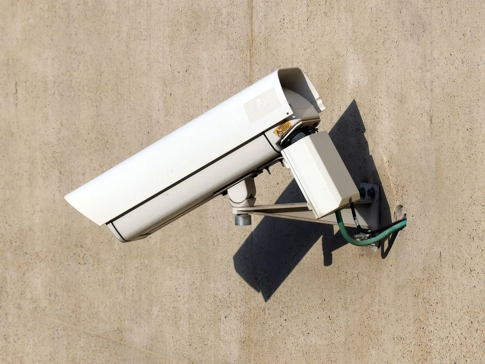 A white security camera mounted on a concrete wall