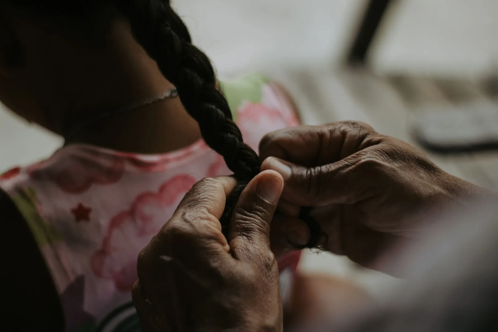 Close-up of adult hands finishing a braid in a young girl's hair and securing the end with a hair tie.