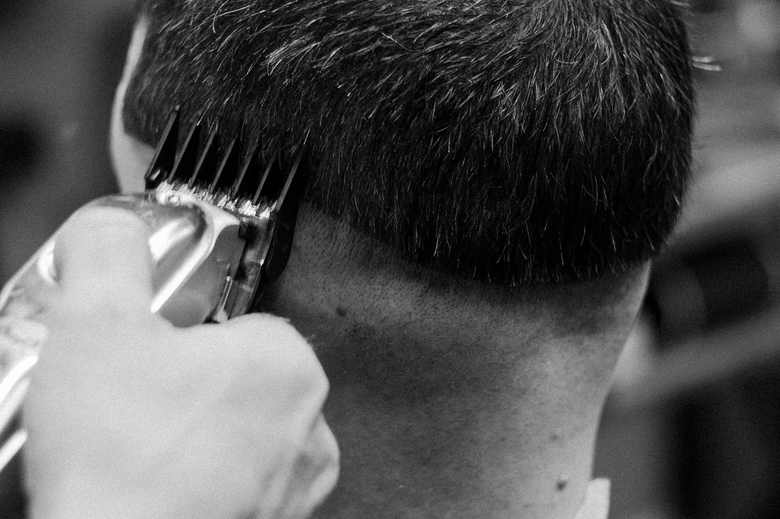 A barber edges up a client's hair with clippers in a close-up black-and-white shot.