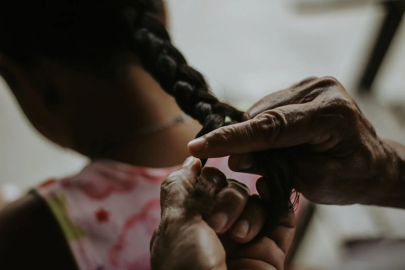 An adult carefully braiding a child's hair indoors