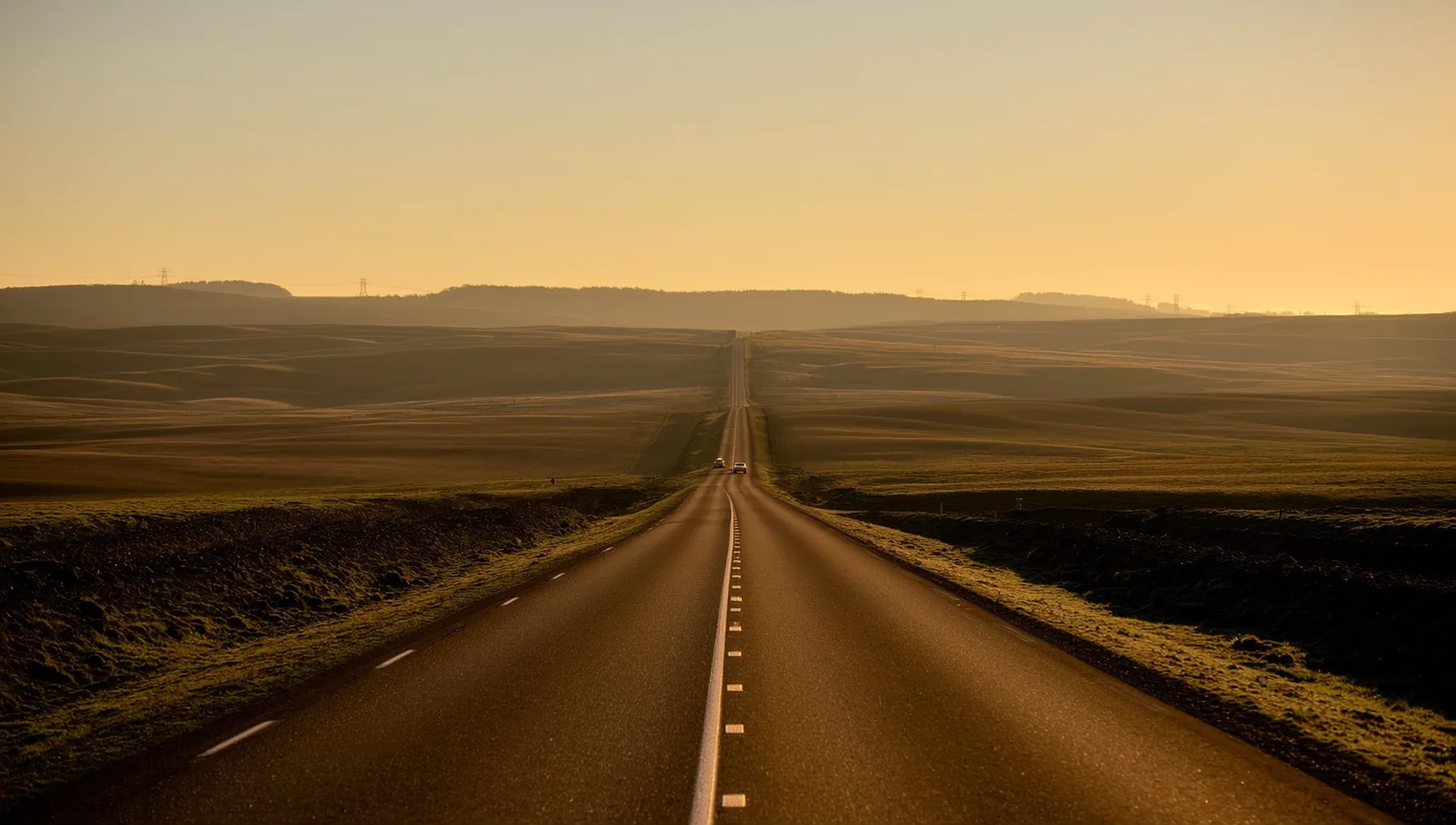 A long empty rural road stretching toward distant hills at golden hour, illustrating the miles many families drive to reach a stylist