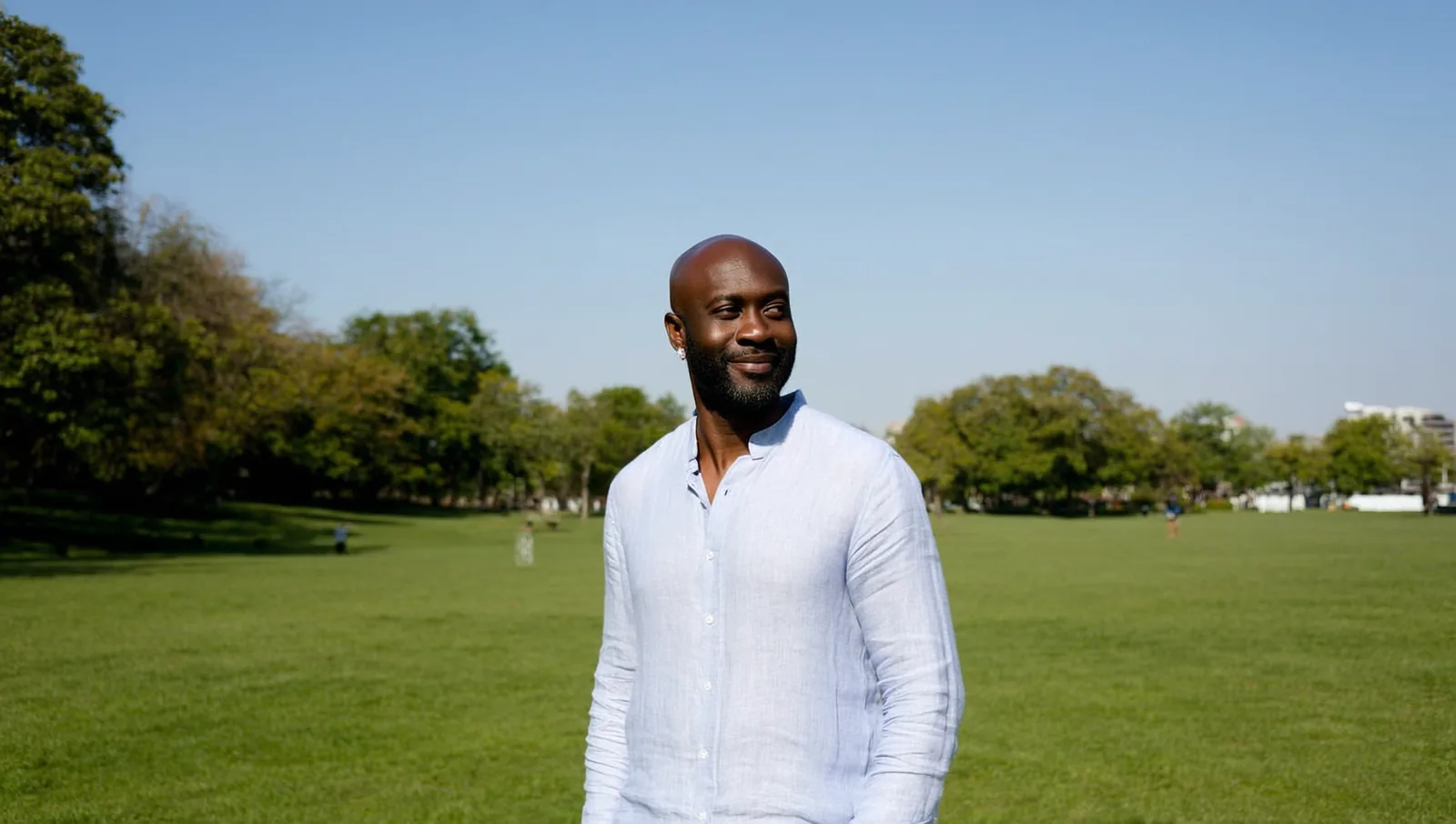 A bald man with a beard standing on park grass