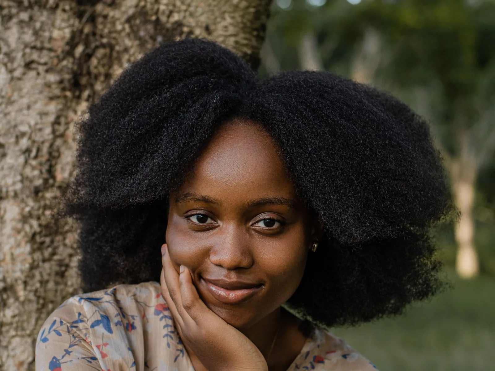 A woman with a large natural afro beside a tree