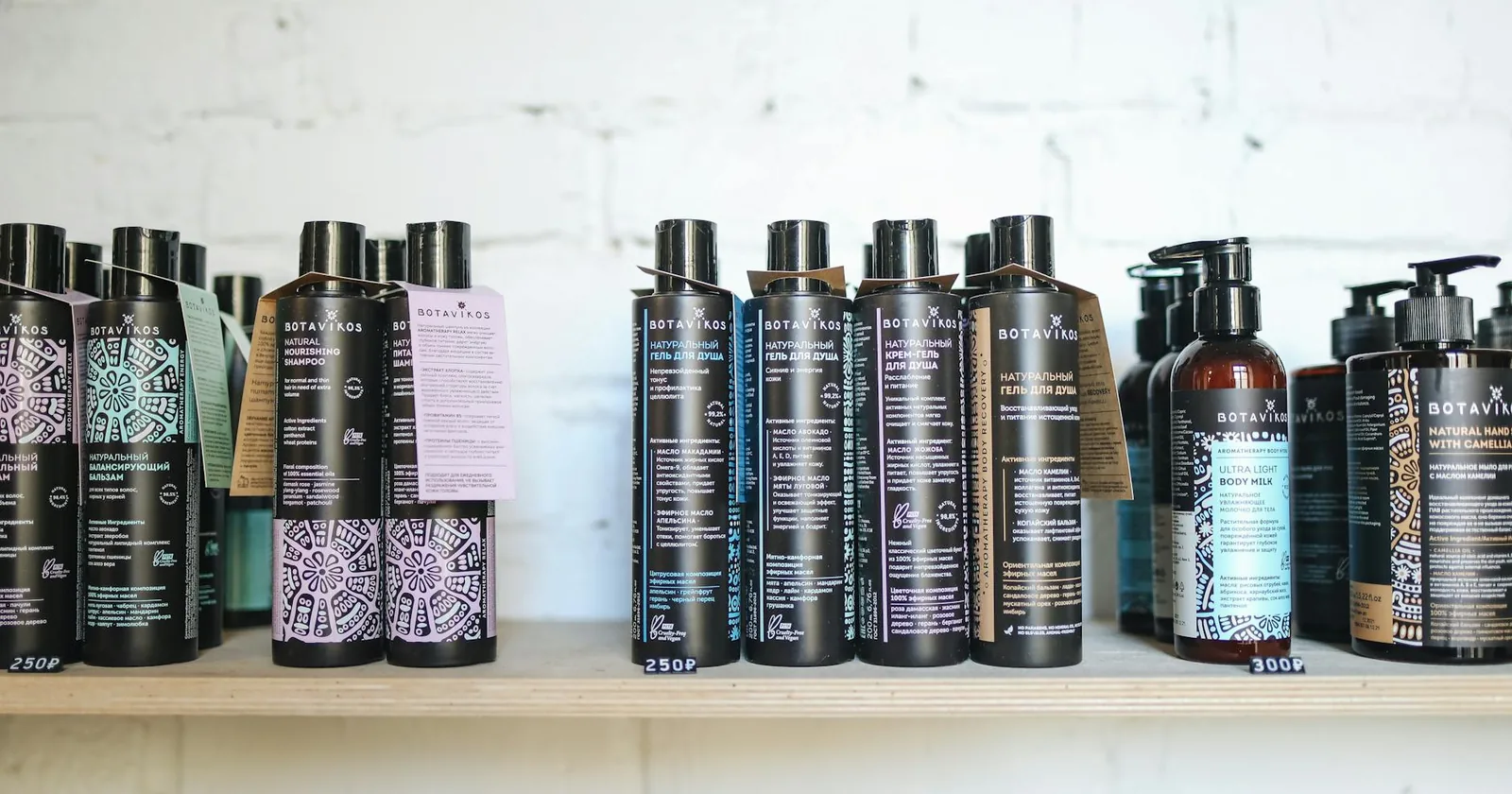 A row of hair care product bottles lined up on a wooden shelf against a white brick wall.